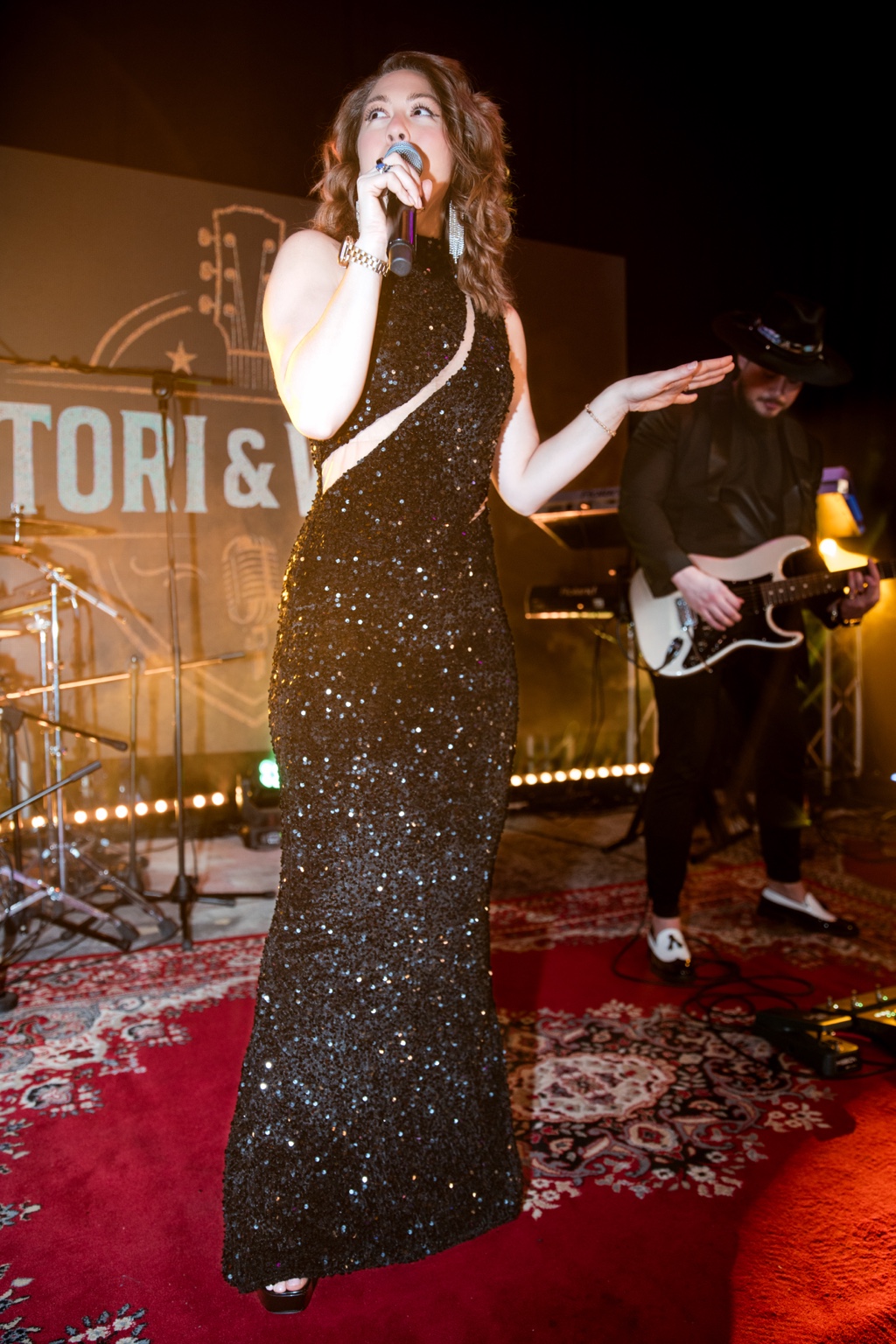 Tori singing in a black sequined dress with Will playing guitar behind her